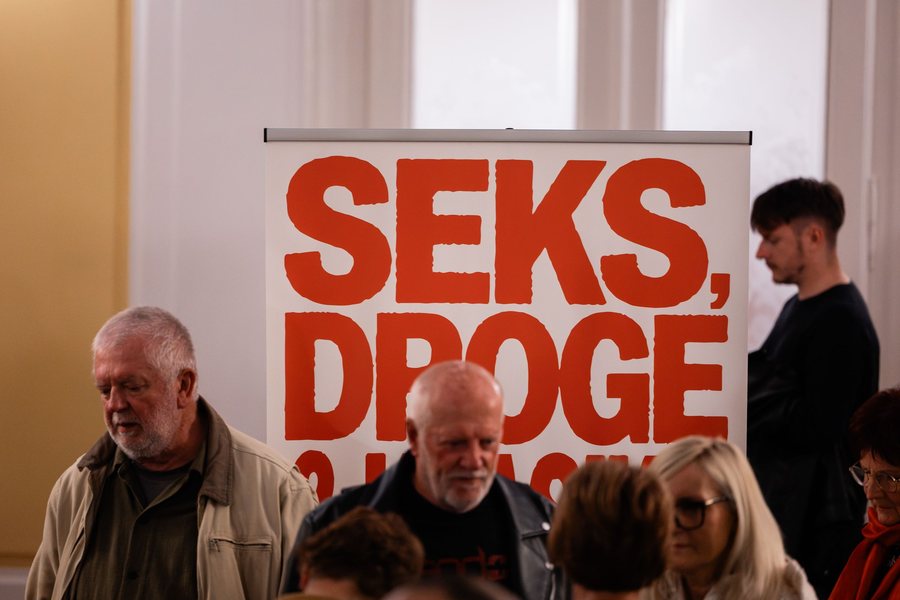 Obiskovalci stojijo pred napisom predstave Seks, droge & klasika v Narodnem domu Celje.